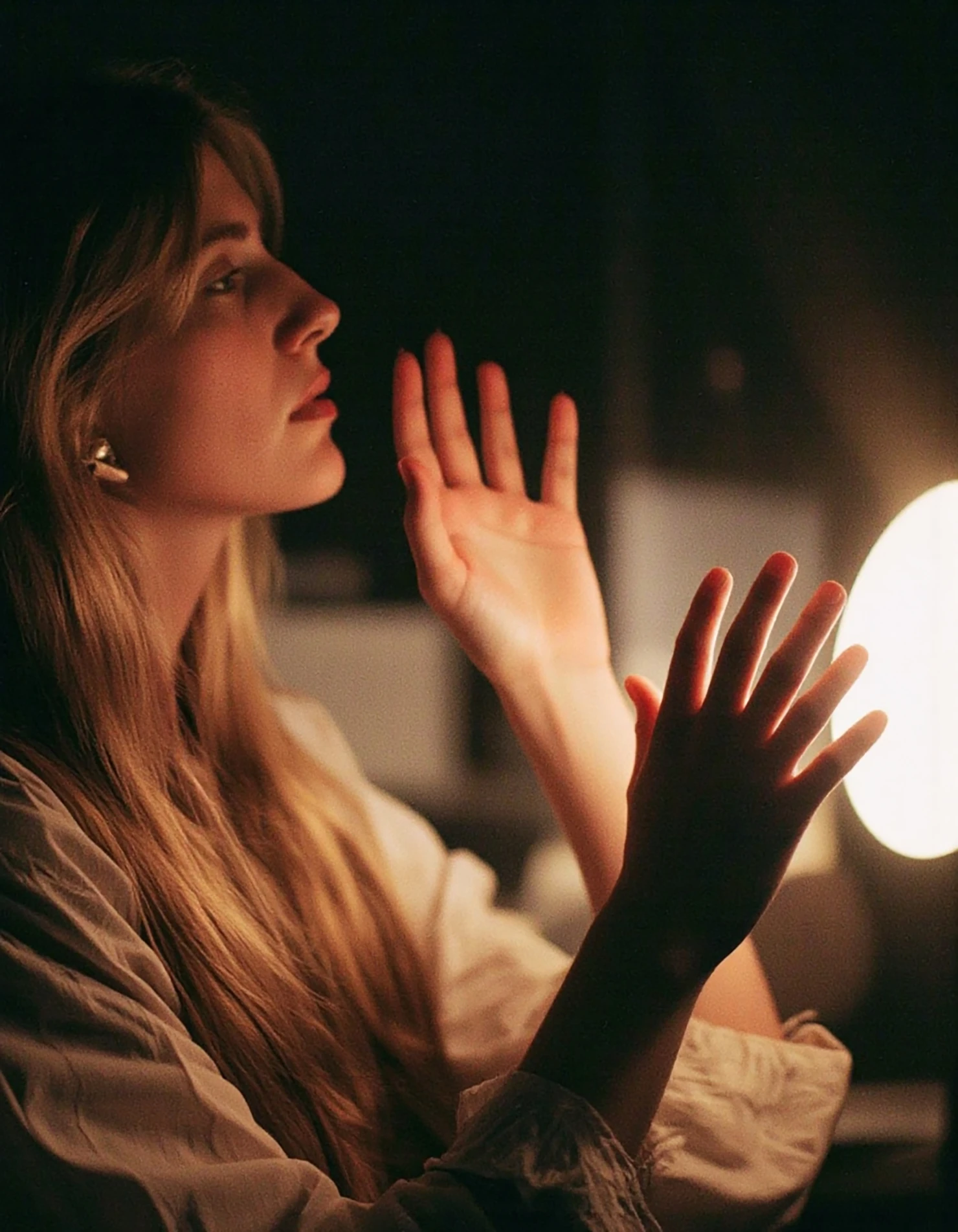 Woman's face illuminated by light and hands, in a dark setting #40105