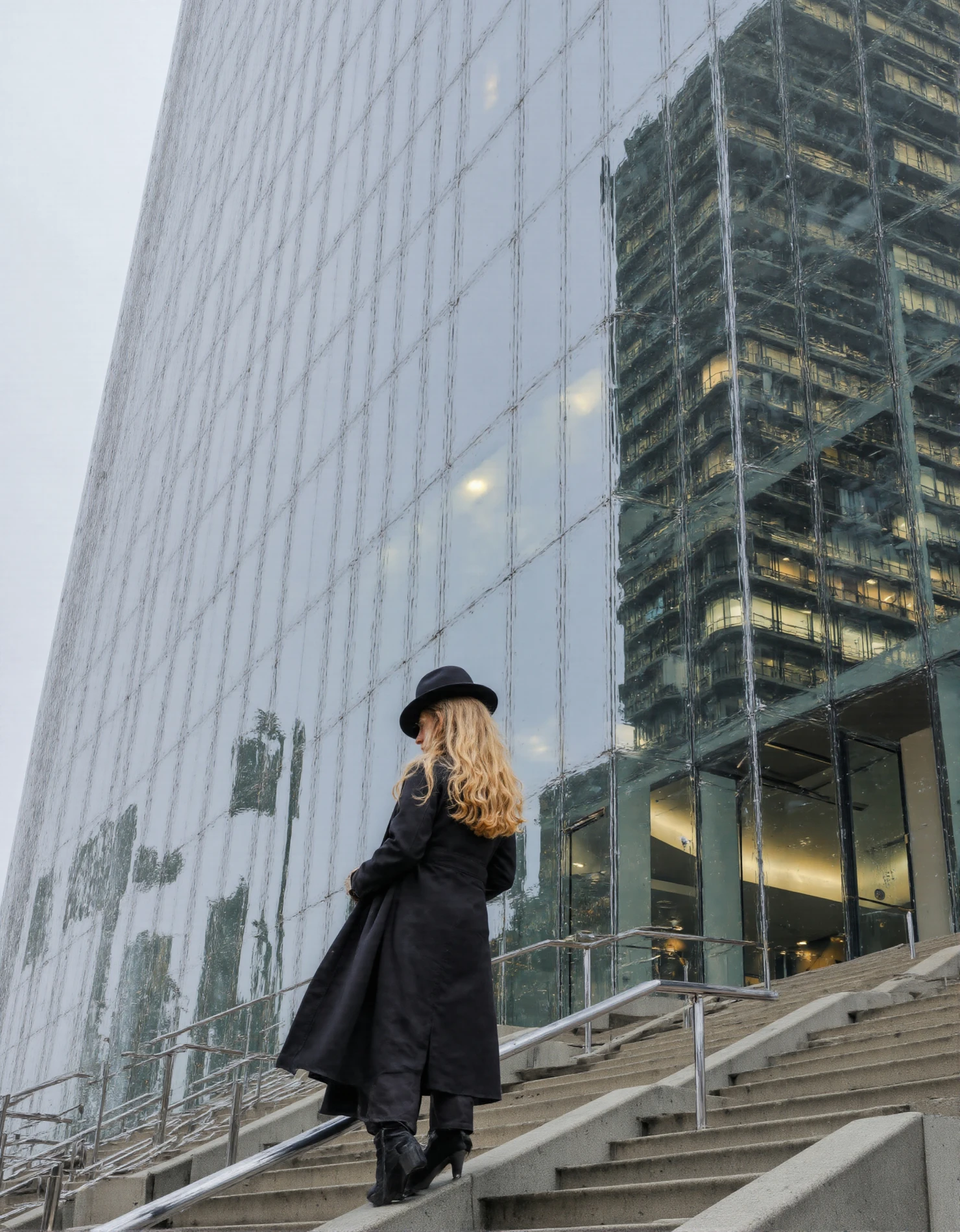 Woman in Black Coat Ascending Stairs Towards a Modern Glass Skyscraper #41218